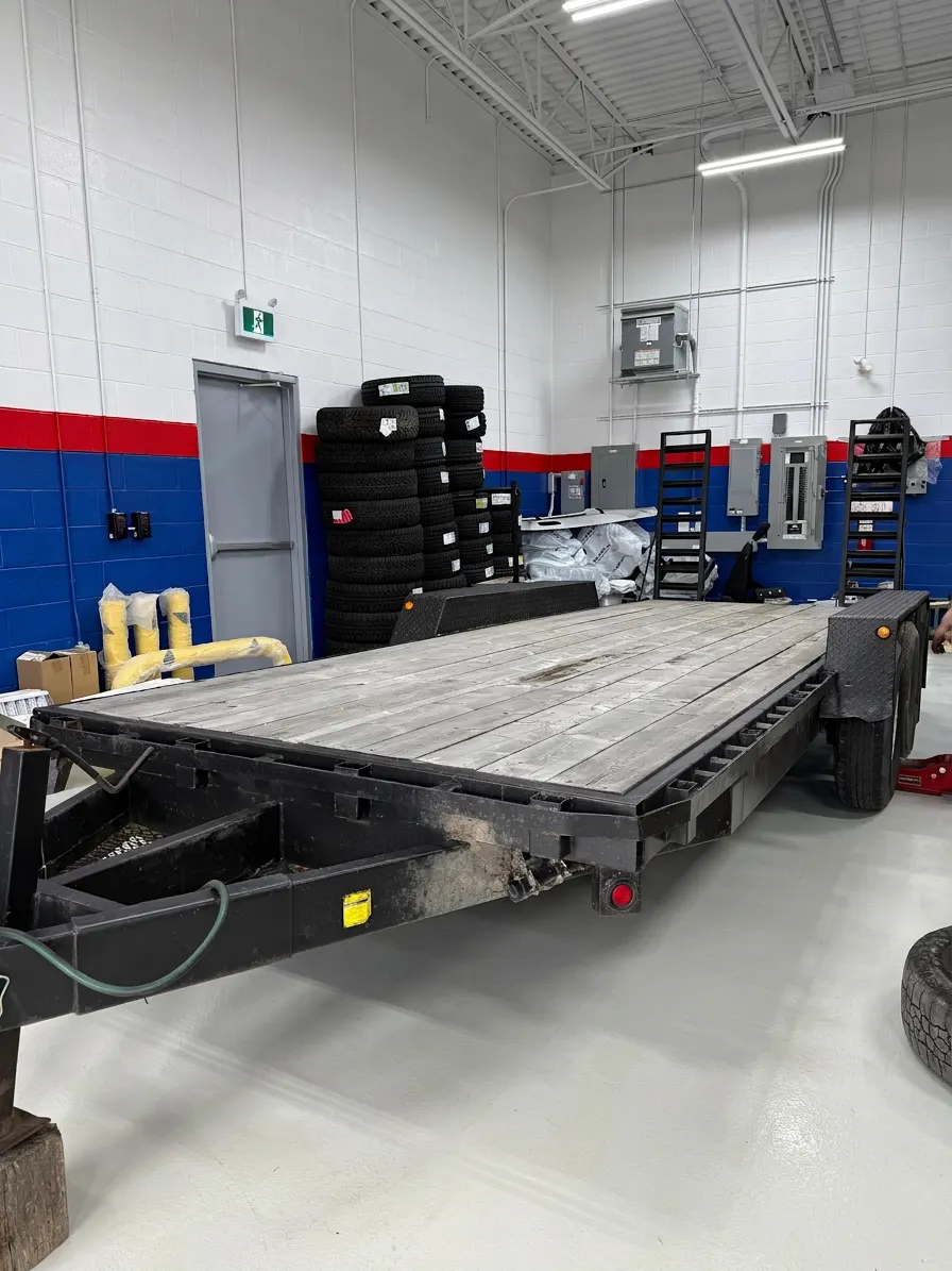 Flatbed trailer in the shop for inspection, with stacks of tires behind it