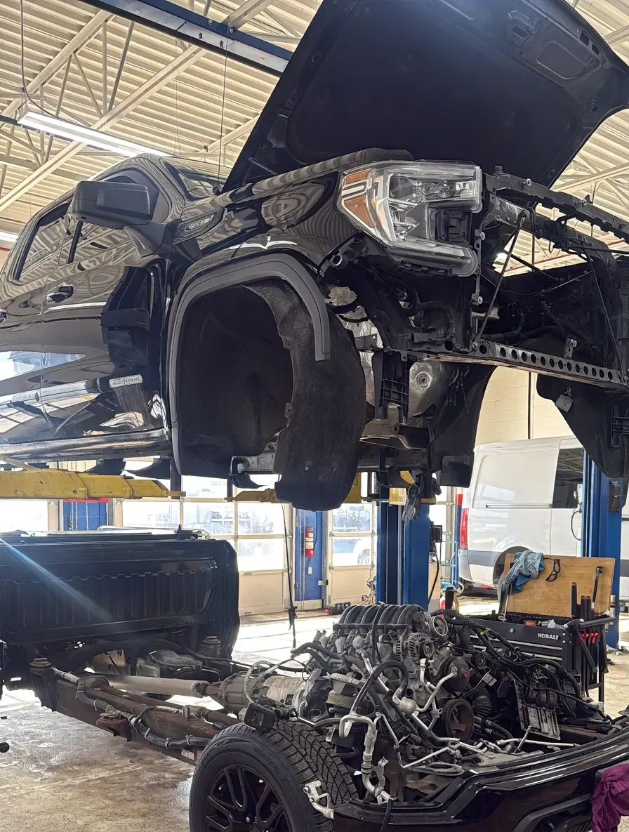Black pickup truck raised on a blue lift with its engine pulled out for repair
