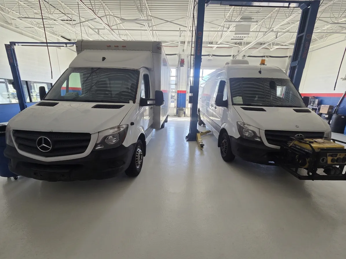 Two white Mercedes Sprinter fleet vans parked between blue lifts